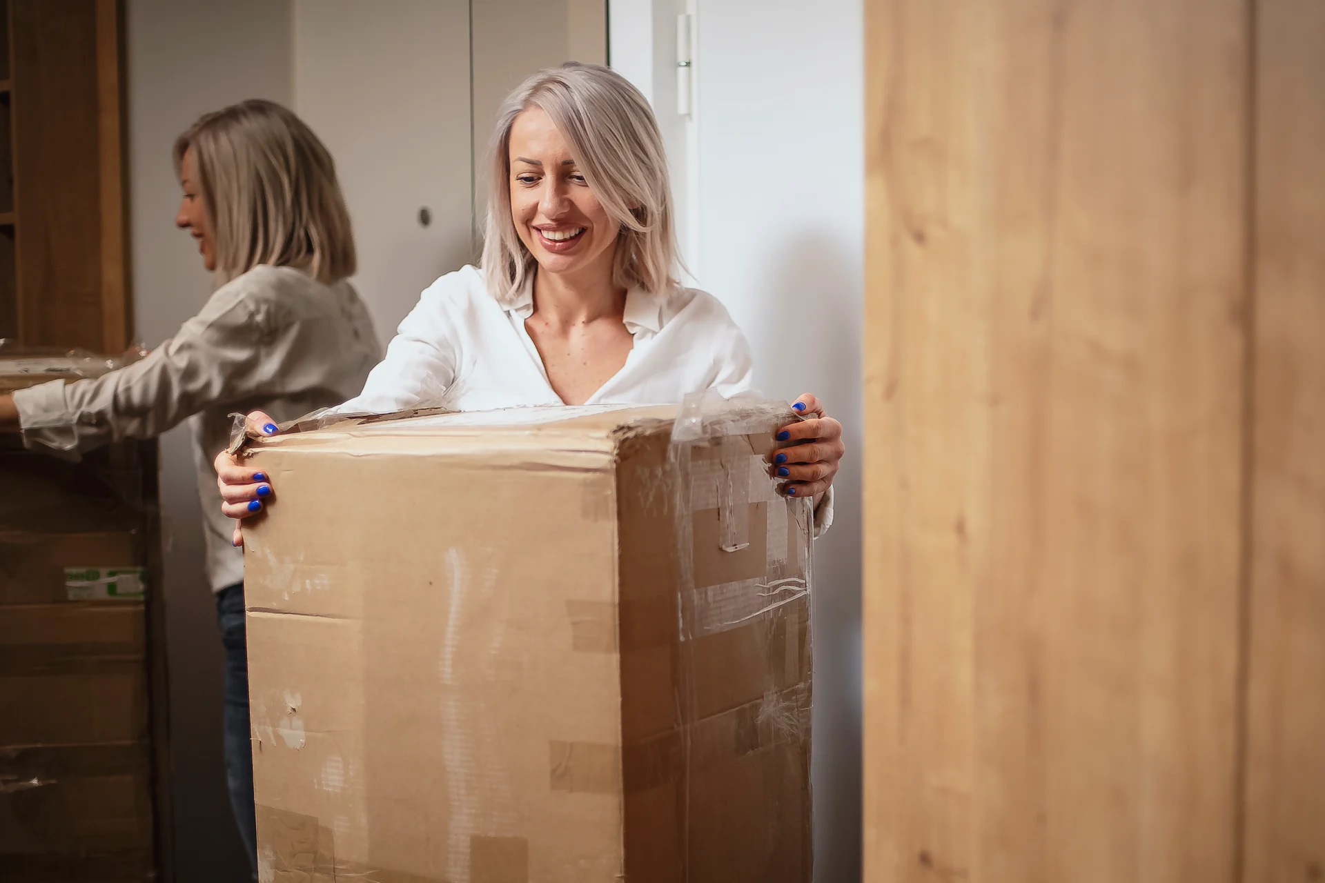 Woman with a smile and blue nail varnish moving a large boxed package
