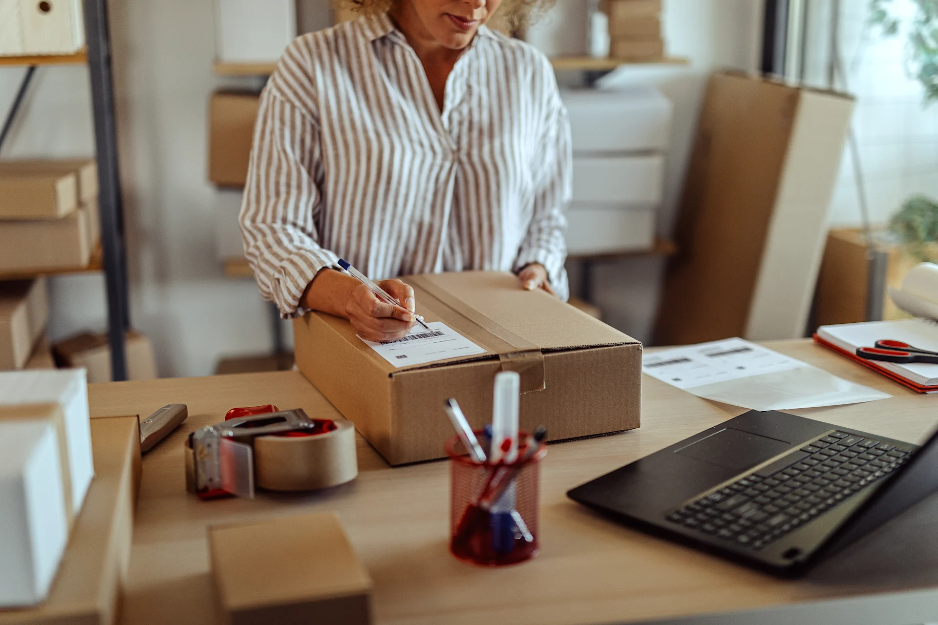 Woman in warehouse holding ballpoint pen to a shipping label