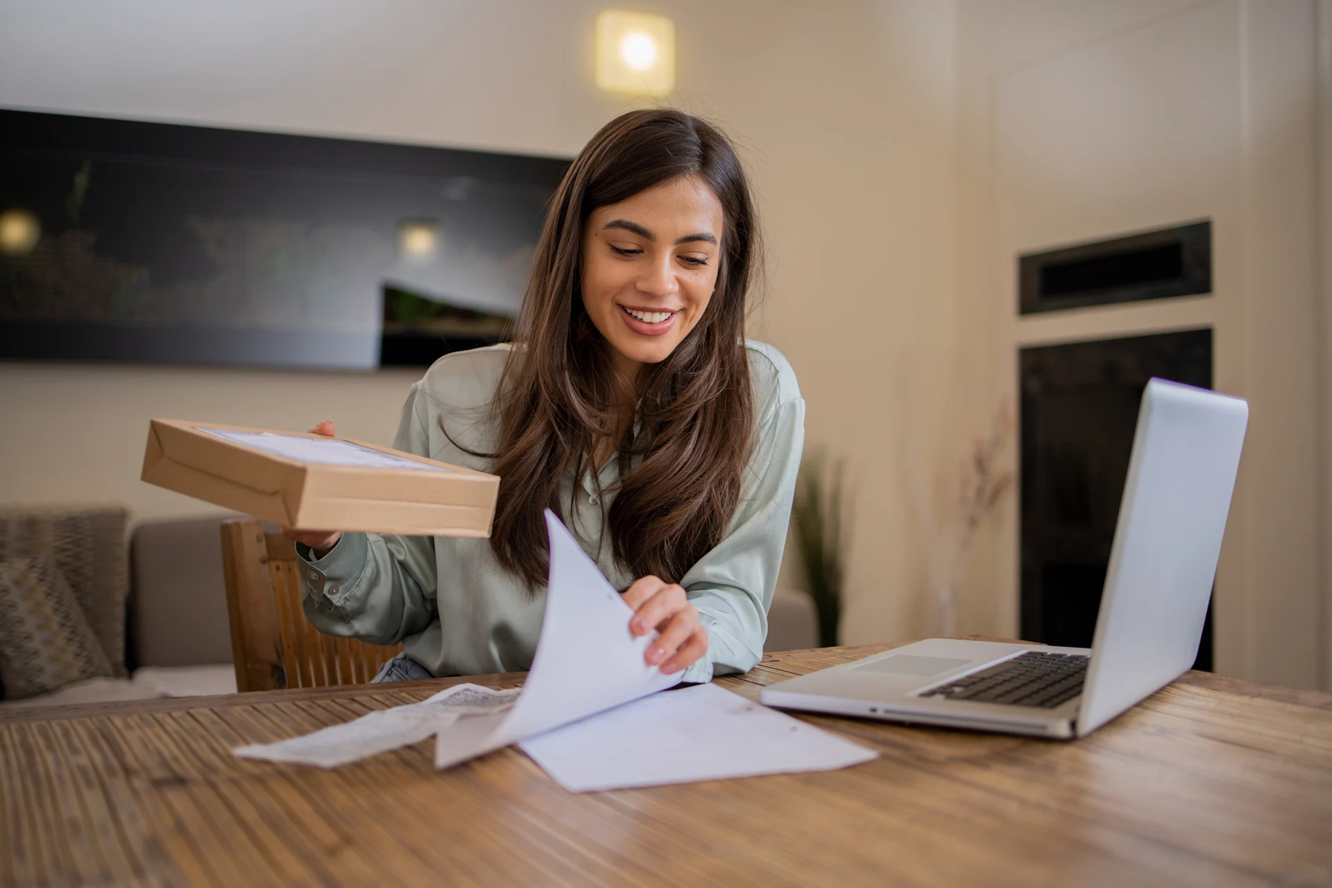 Woman smiling while using laptop and holding parcel